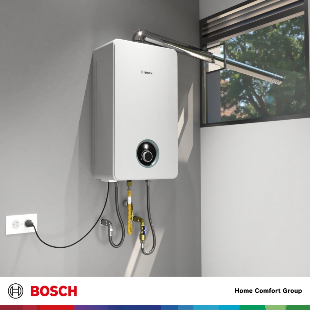 White Bosch tank style water heater mounted on a gray wall with exposed pipes and a window above Bosch logo visible on the unit