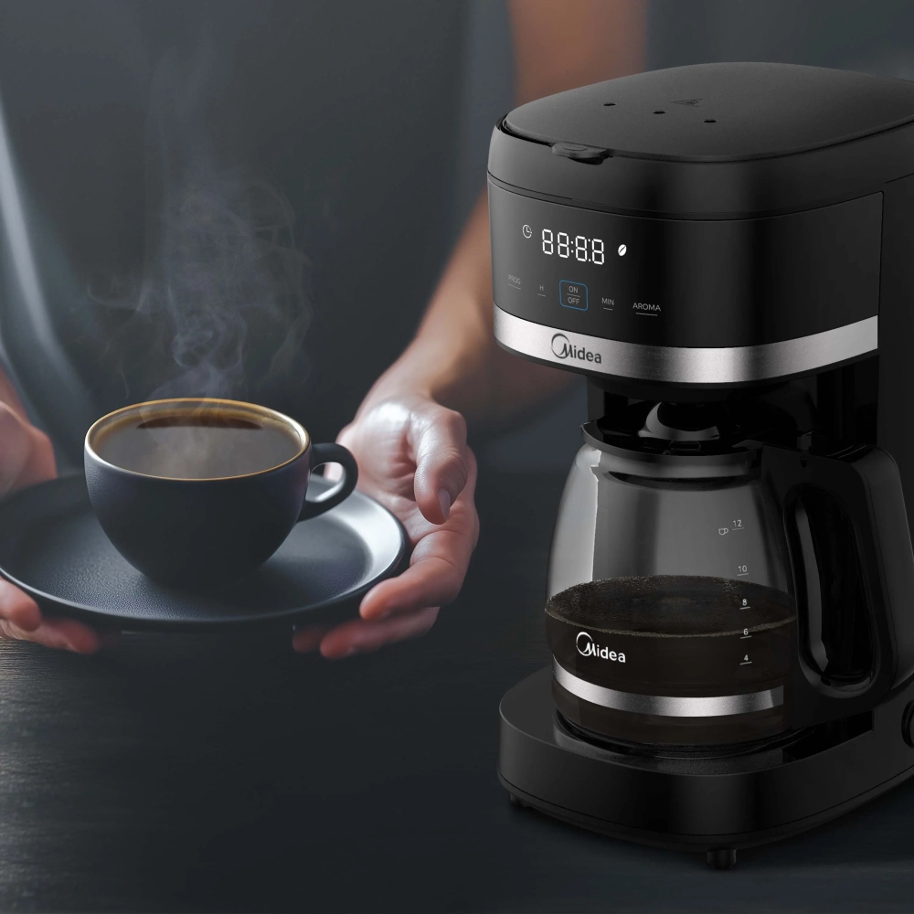 Person holding a steaming black coffee cup on a saucer beside a black drip coffee maker